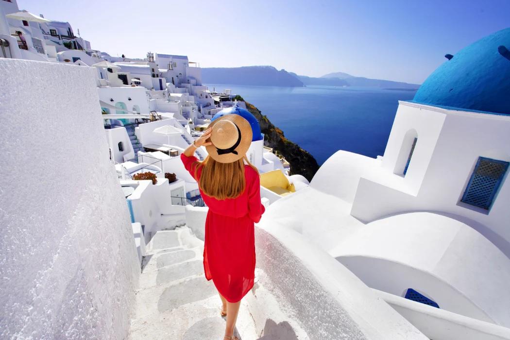 Beautiful girl in red dress and hat comes down the stairs exploring Oia village - Santorini Beautiful girl in red dress and hat comes down the stairs exploring Oia village - Santorini